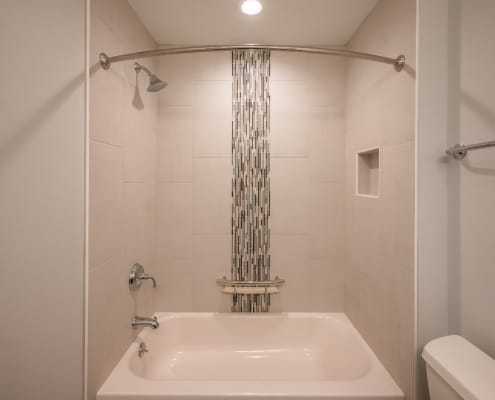 Vertical glass tile feature in shower stall with curved shower curtain bar in McLean, VA bathroom remodel