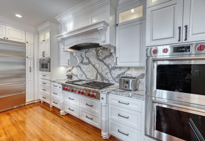 Custom Crystal cabinetry painted white with Wolf range and wall ovens with red knobs and