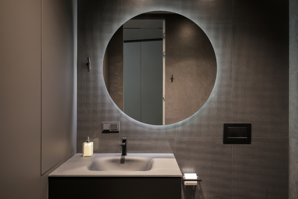 Illuminated round mirror in a dark bathroom interior