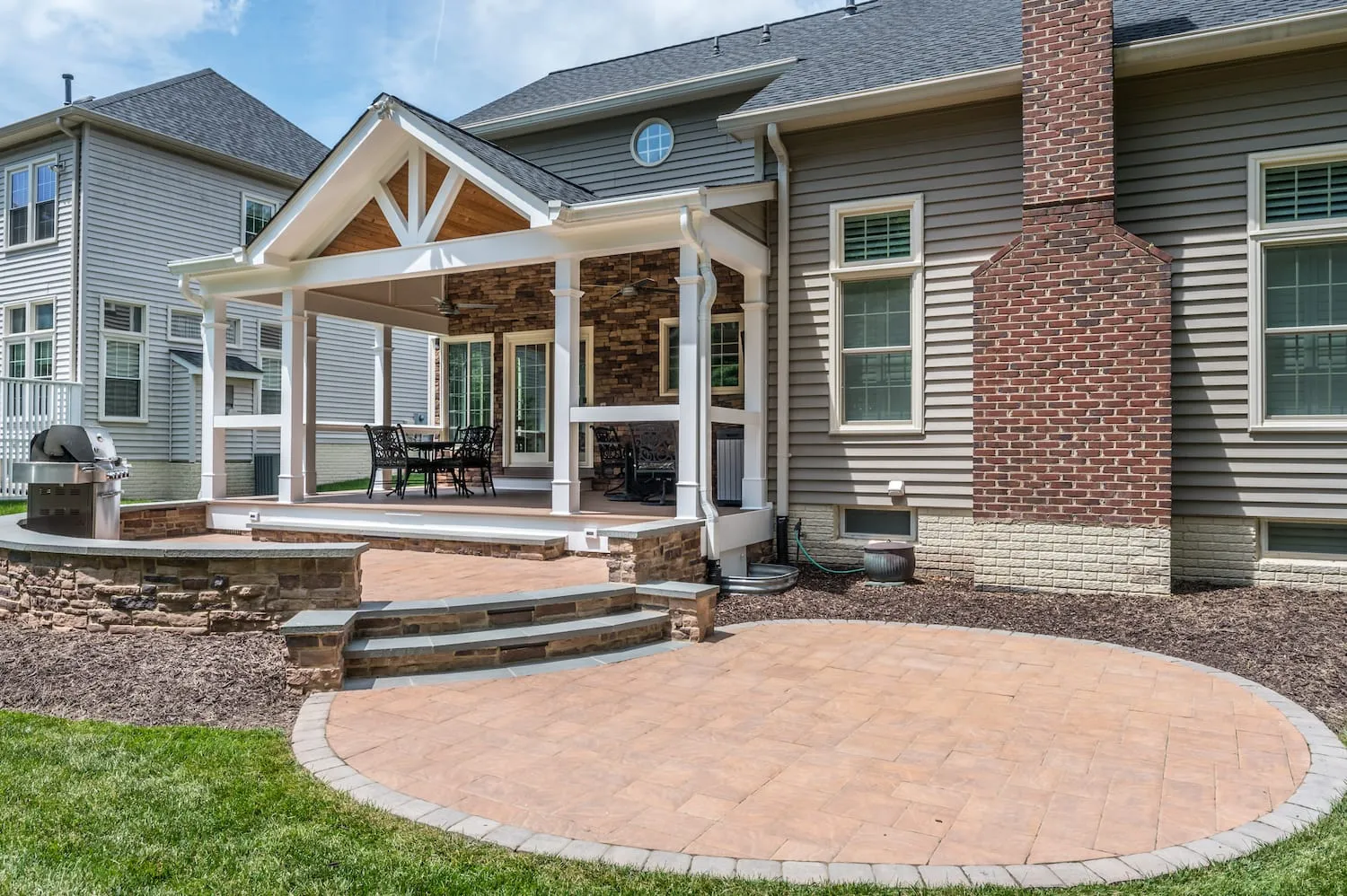 Custom circular brick patio in front of a small home with covered front porch and gray and brick siding.